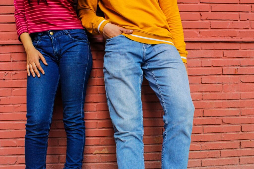 2 people wearing jeans in front of a brick wall. One pair is dark and skinny, one pair is light and baggy.