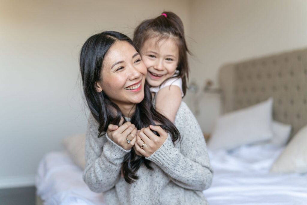 Mother and daughter play on clean bed in clean clothes