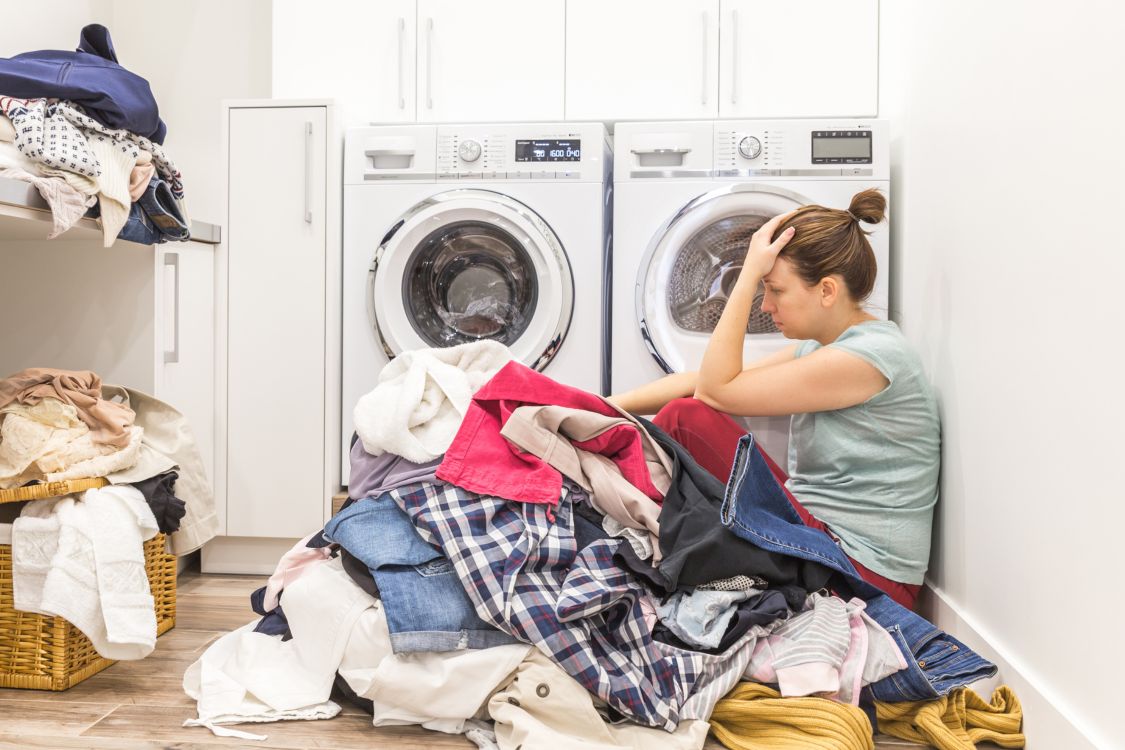 Mom sits among a pile of laundry, looking overwhelmed