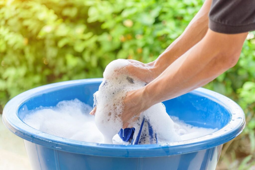 man handwashing swimsuit in a bucket