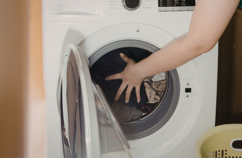 hand shoving too much laundry into washing machine